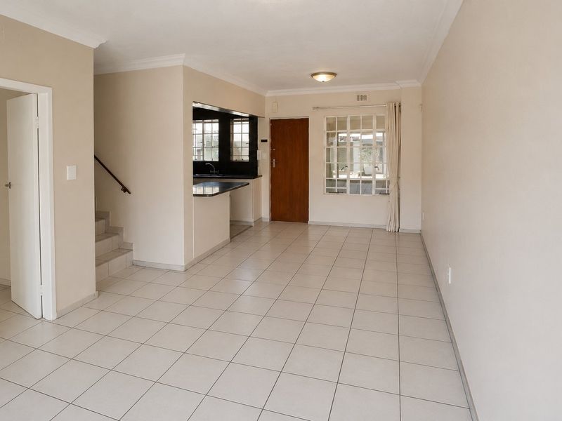An open-plan living area featuring neutral tiled flooring, a staircase, and a kitchen pass-through, offering a clean and versatile space.