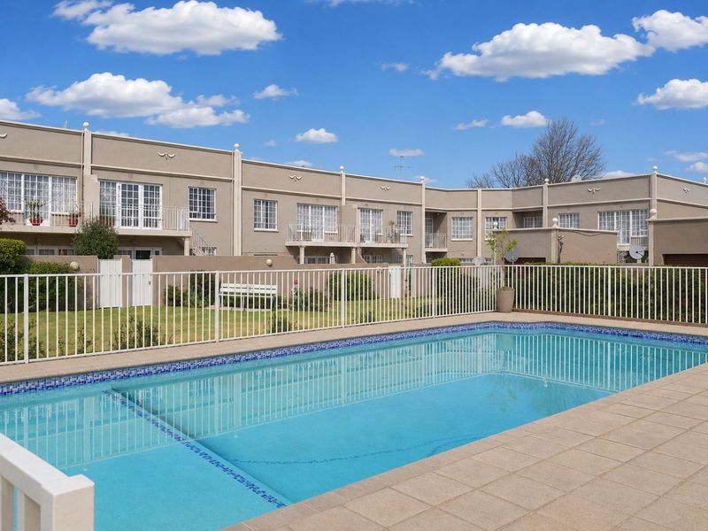 A well-maintained communal swimming pool area featuring a tiled surround and metal fencing, set against the rear facade of a townhouse complex.