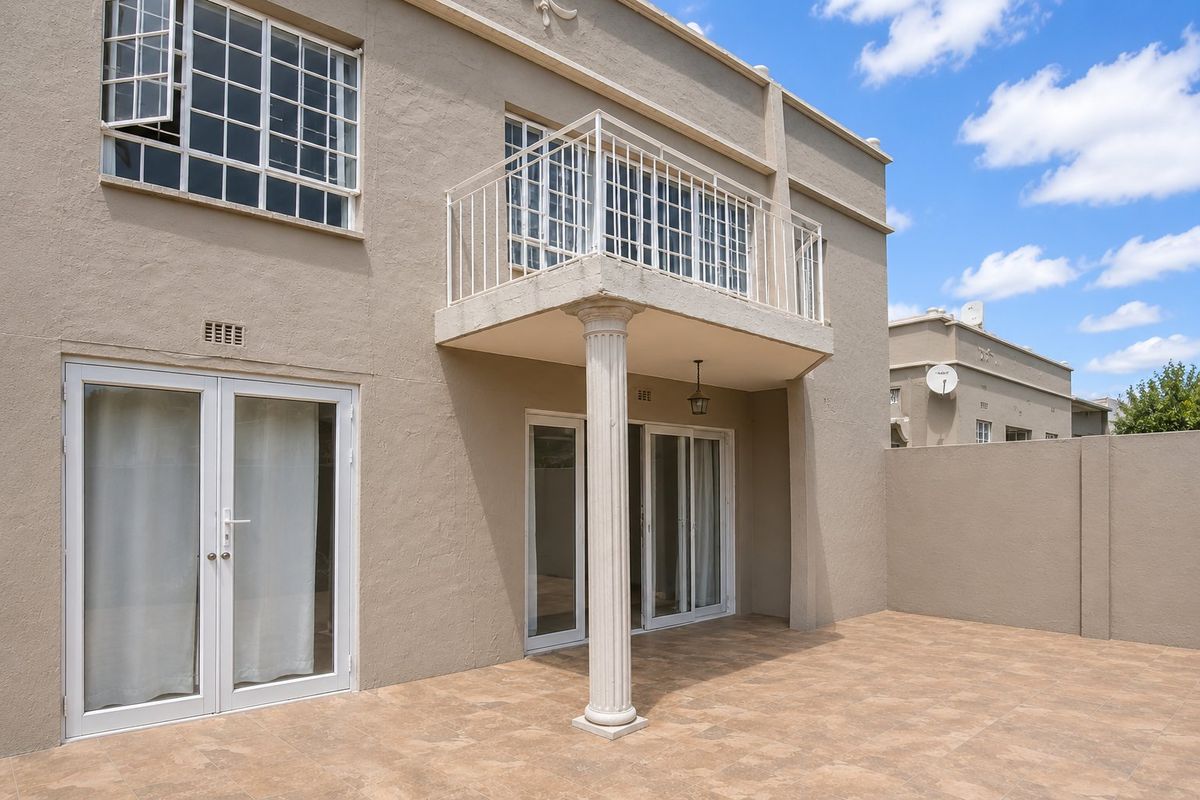 Rear exterior view of the townhouse featuring a tiled patio, a balcony supported by a column, and multiple glass door access points.
