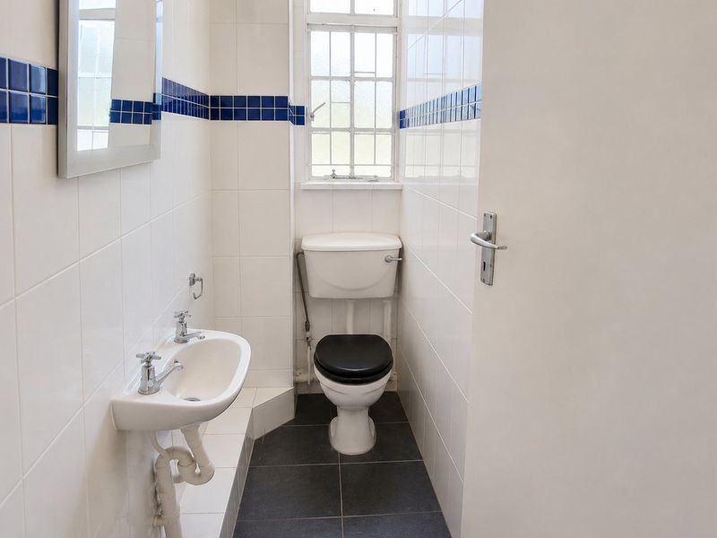 A compact, functional bathroom featuring white wall tiles with blue accents, a wall-mounted basin, and a toilet.