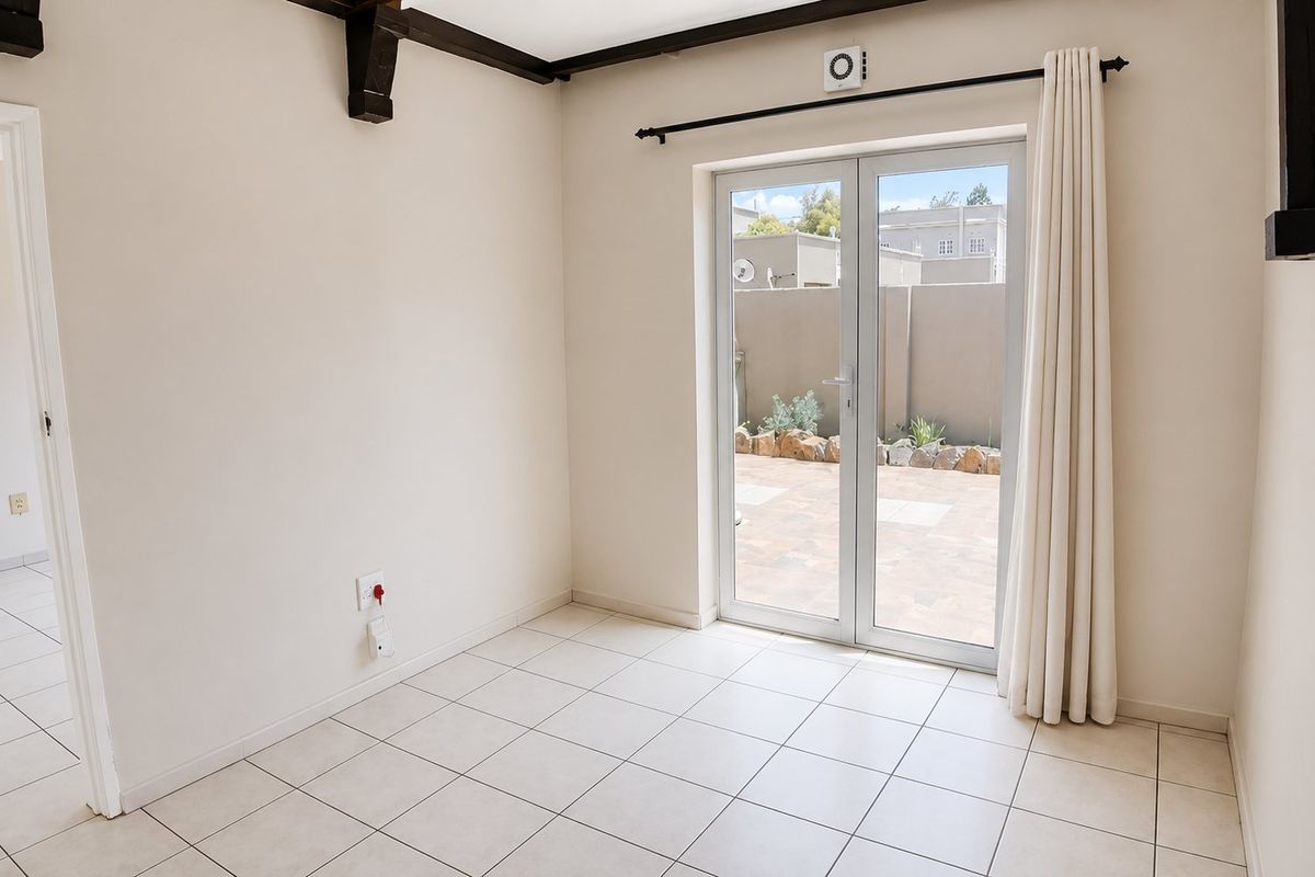An empty living room featuring tiled flooring, exposed ceiling beams, and double glass doors providing direct access to the rear patio area.