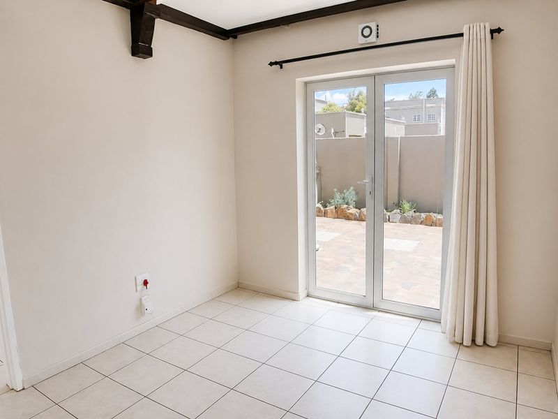 An empty living room featuring tiled flooring, exposed ceiling beams, and double glass doors providing direct access to the rear patio area.