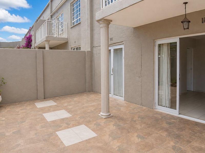 A covered patio area featuring tiled flooring, a decorative column, and sliding glass doors providing access to the interior living space.