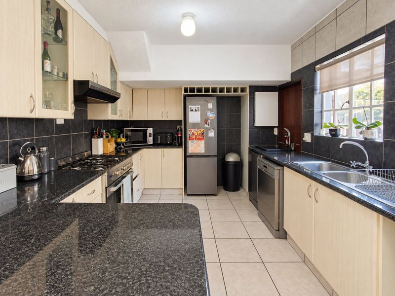 A functional kitchen featuring granite countertops, light wood cabinetry, a gas hob, and tiled finishes throughout.