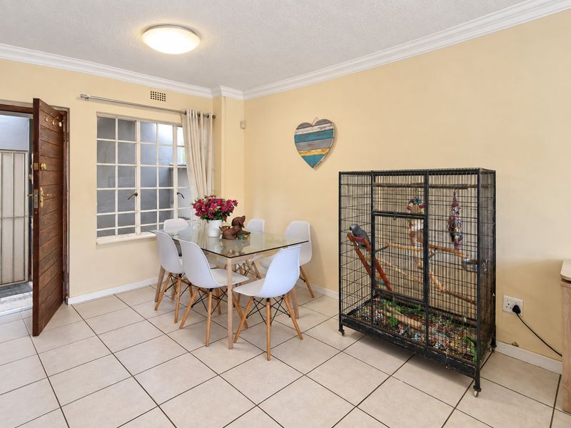 A functional dining area featuring tiled flooring, decorative ceiling cornicing, and a grid-style window providing natural light, with direct access to an exterior space.