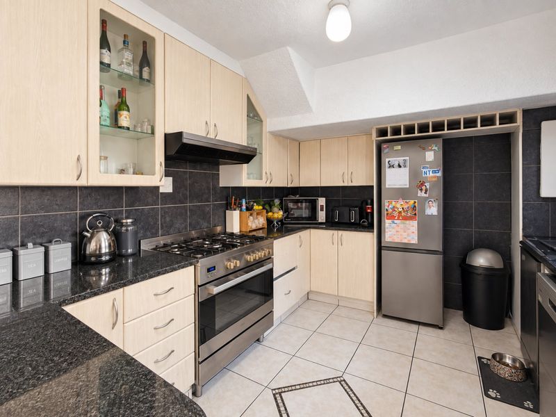 A functional kitchen featuring light wood cabinetry, dark granite countertops, a gas stove with extractor fan, and tiled flooring with a decorative inlay.