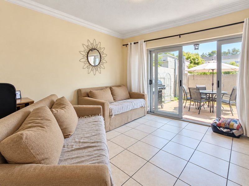 A bright living room featuring ceramic floor tiles, crown molding, and large sliding glass doors providing direct access to the outdoor patio area.