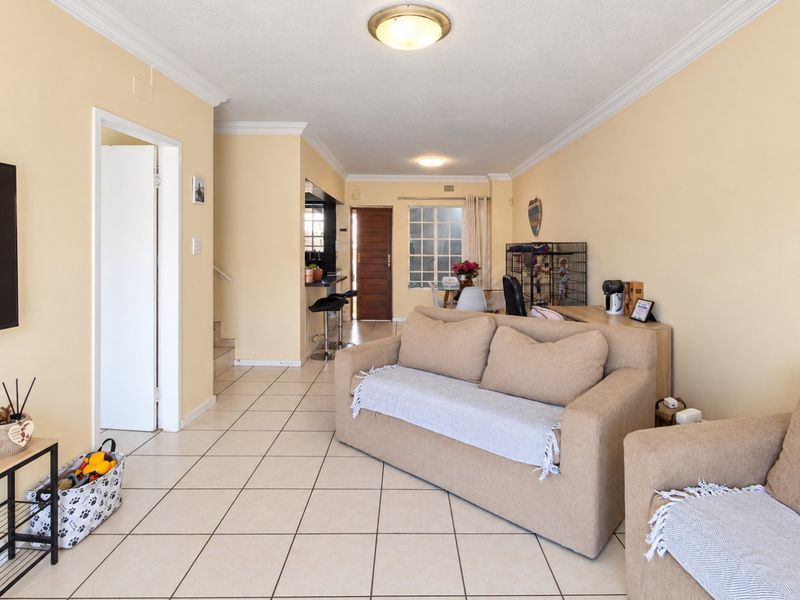 Open-plan living area featuring tiled flooring, neutral wall tones, and a breakfast bar connecting to the kitchen space.