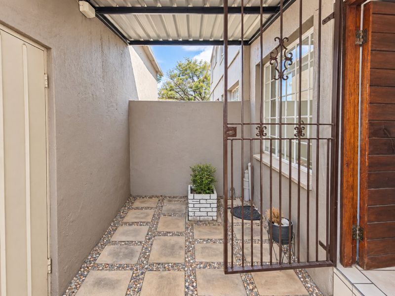 A small, covered outdoor patio area featuring paved flooring with pebble accents, enclosed by a metal security gate and exterior walls.