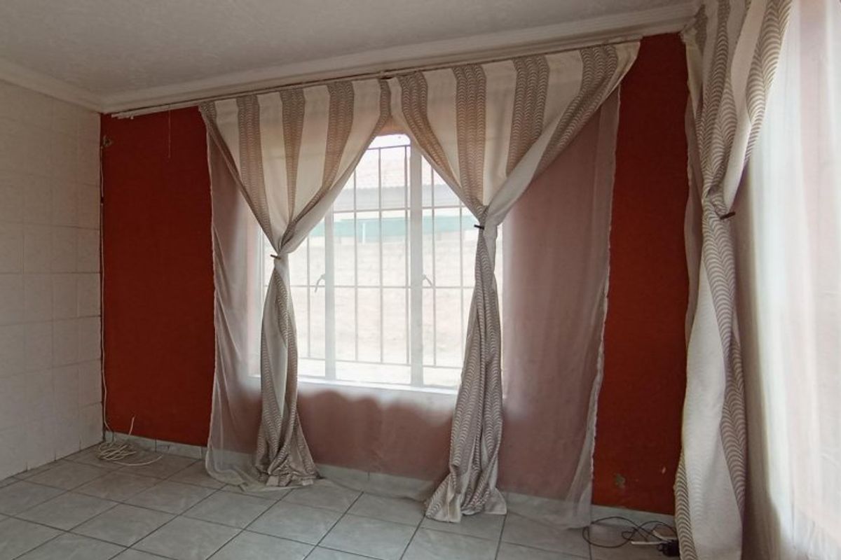 An empty living room featuring tiled flooring, security bars on the windows, and decorative coving, ready for a fresh update.