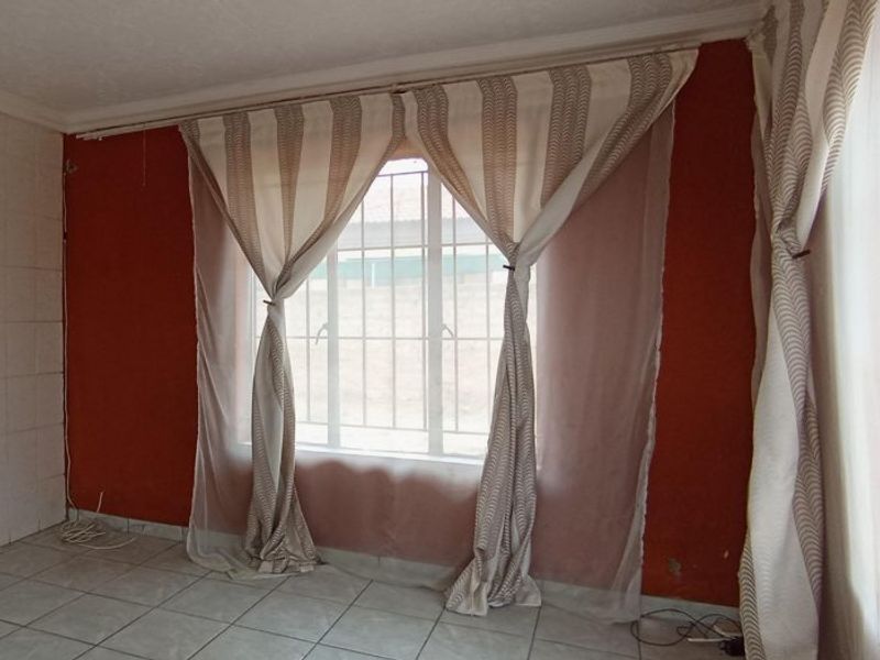 An empty living room featuring tiled flooring, security bars on the windows, and decorative coving, ready for a fresh update.