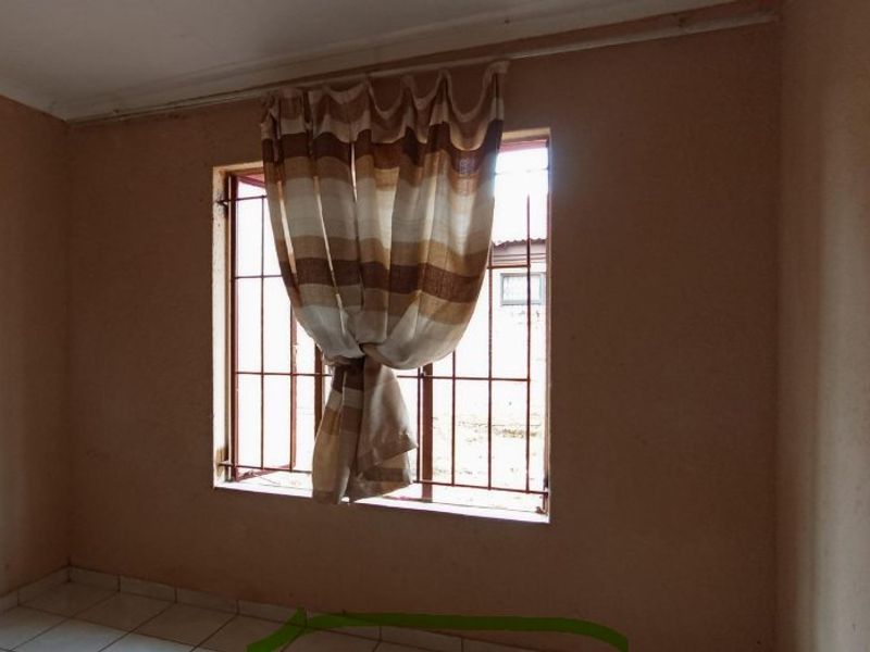 A vacant bedroom featuring tiled flooring, security bars on the window, and plain wall finishes, offering a blank canvas for potential updates.