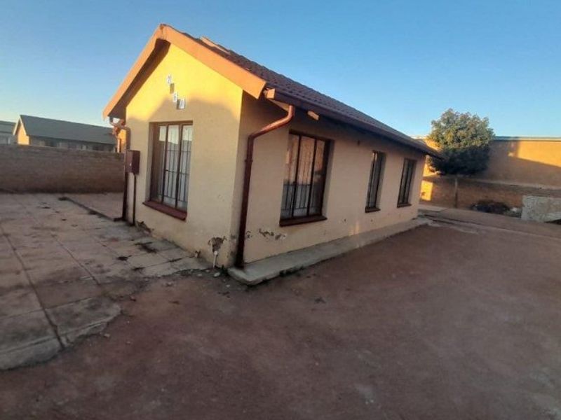 Rear view of a detached house featuring a tiled roof, security bars on windows, and a paved yard area requiring maintenance.
