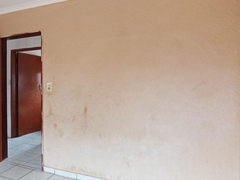 An empty bedroom featuring tiled flooring and textured walls, showing signs of wear and requiring cosmetic updates.
