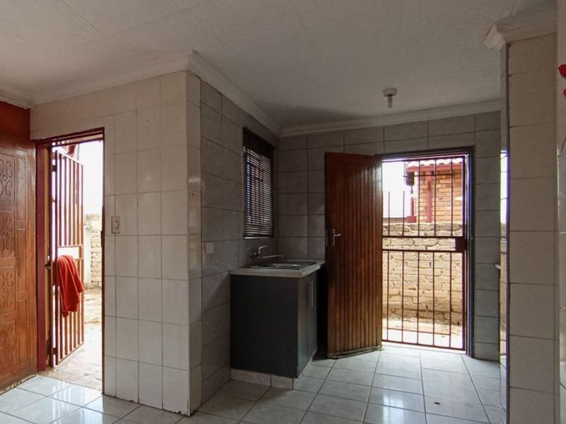 A functional scullery or utility area featuring tiled walls and flooring, a built-in sink, and direct access to the exterior via security gates.