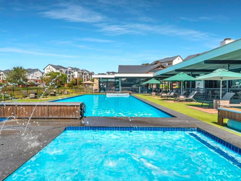 A well-maintained communal swimming pool area featuring a water feature, tiled surrounds, and an adjacent covered patio space within the apartment complex.