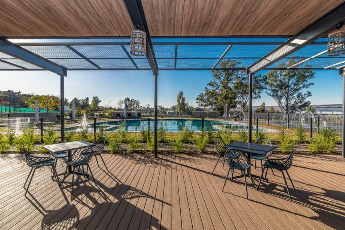 A well-maintained outdoor pool area featuring timber decking, a modern metal pergola, and a clear swimming pool with landscaped surroundings.