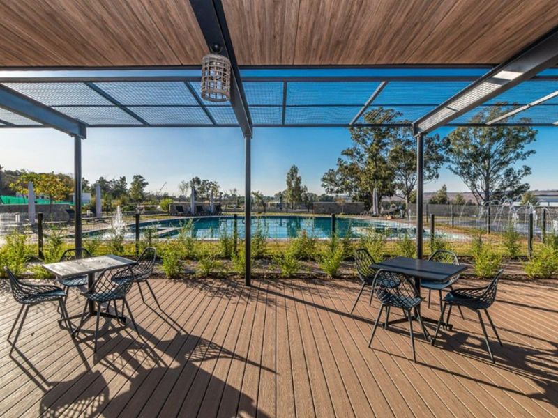 A well-maintained outdoor pool area featuring timber decking, a modern metal pergola, and a clear swimming pool with landscaped surroundings.