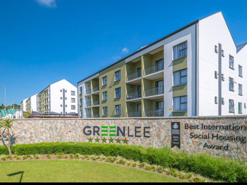 Exterior view of the Greenlee apartment complex featuring modern multi-story architecture, private balconies, and a landscaped entrance with stone boundary wall.