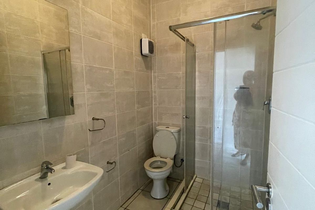 A clean, neutral-toned bathroom featuring a pedestal basin, toilet, and a glass-enclosed shower with full-height wall tiling.
