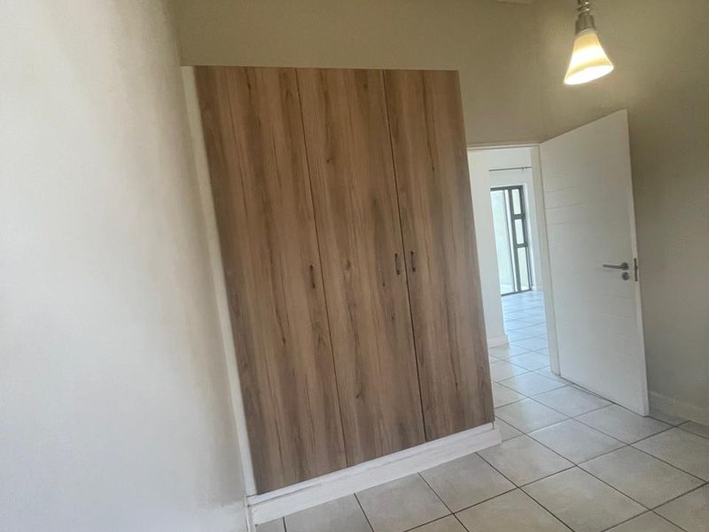 A clean, empty bedroom featuring neutral tiled flooring, a modern wood-finish built-in wardrobe, and a simple pendant light fixture.
