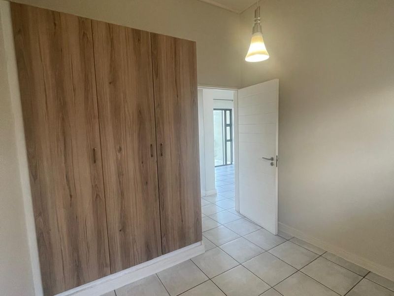 A clean, empty bedroom featuring modern wood-finish built-in cupboards, neutral tiled flooring, and a simple pendant light fixture.