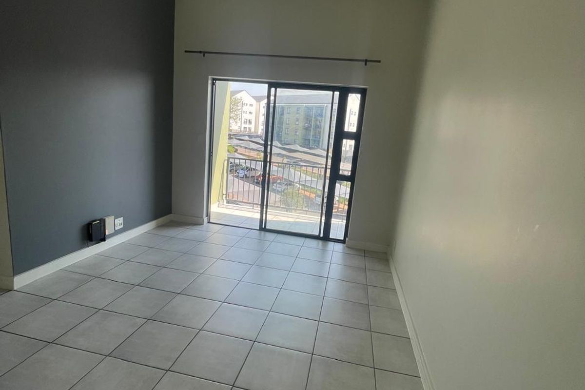 An empty living room featuring neutral tiled flooring, a dark grey accent wall, and a sliding glass door providing access to a balcony.