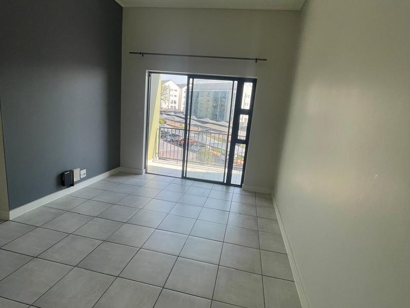 An empty living room featuring neutral tiled flooring, a dark grey accent wall, and a sliding glass door providing access to a balcony.