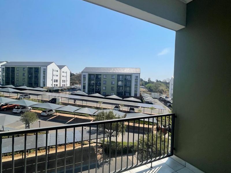 A clean, tiled balcony featuring a metal balustrade with an open view overlooking the apartment complex parking area.