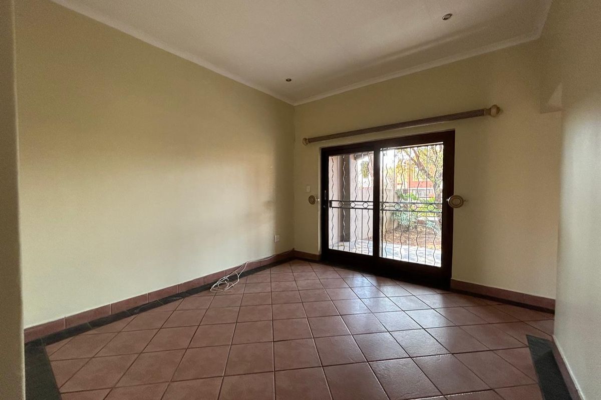 An empty living room featuring tiled flooring, recessed lighting, and a sliding glass door with a security gate leading to the exterior.