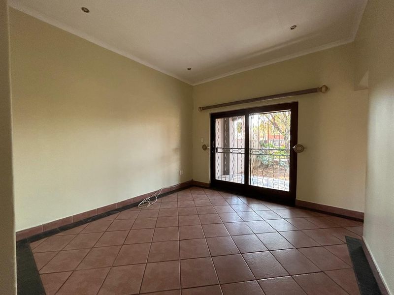 An empty living room featuring tiled flooring, recessed lighting, and a sliding glass door with a security gate leading to the exterior.