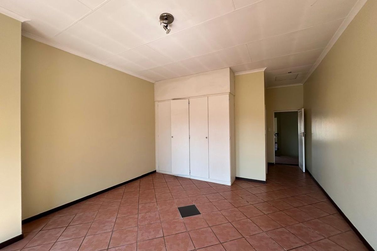 An empty bedroom featuring tiled flooring, built-in cupboards, and a central ceiling light fixture.
