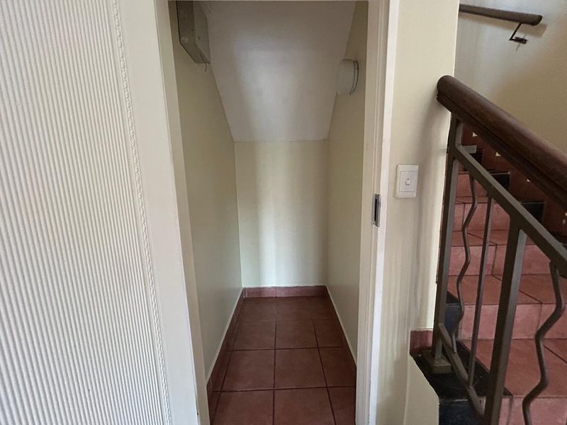 A compact under-stair storage area featuring tiled flooring, located adjacent to the main staircase with a metal handrail.