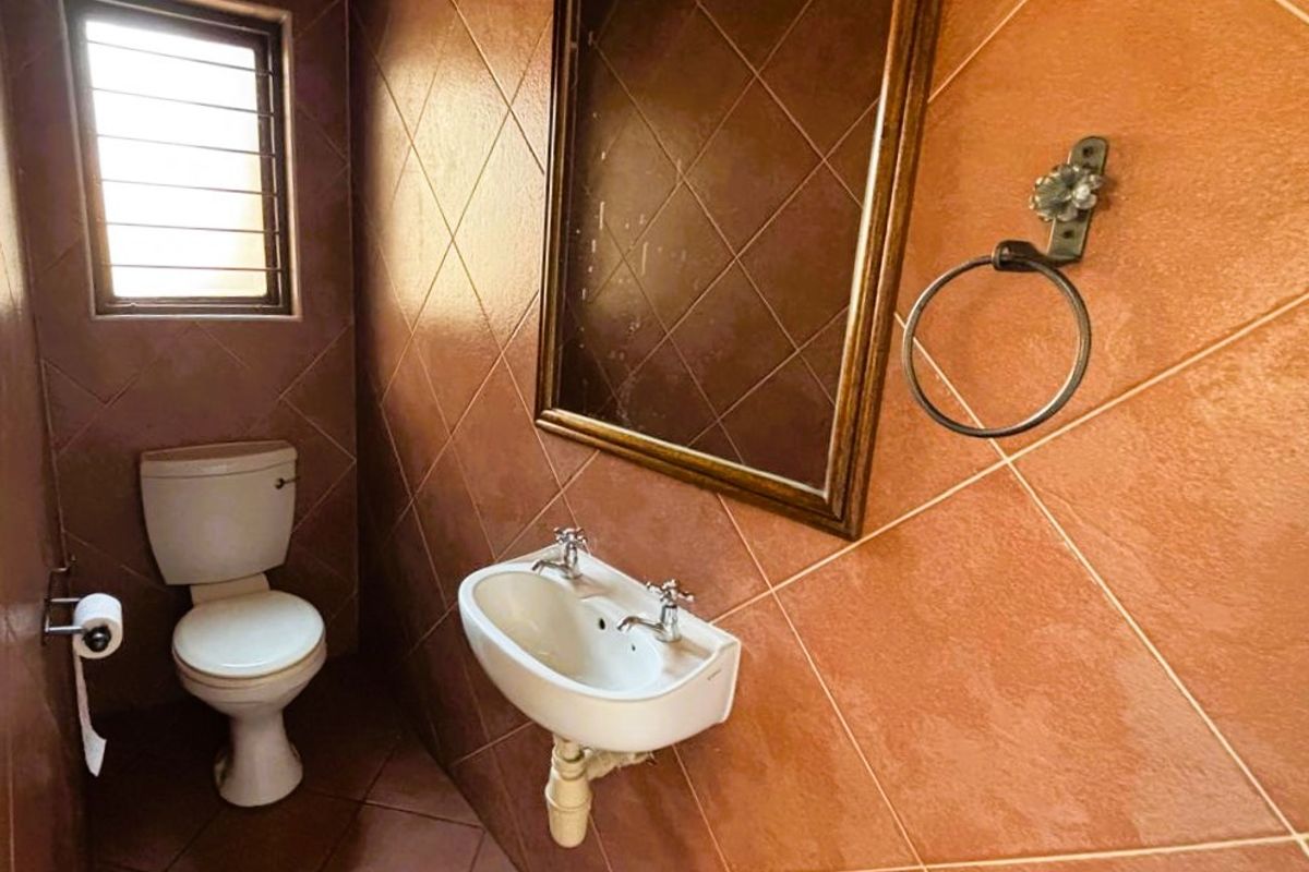 A compact guest bathroom featuring tiled walls, a wall-mounted basin, and a standard toilet, currently in a dated condition.