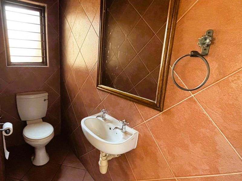 A compact guest bathroom featuring tiled walls, a wall-mounted basin, and a standard toilet, currently in a dated condition.