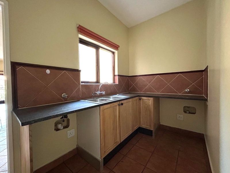 A functional laundry room featuring built-in wooden cabinetry, a double basin sink, and tiled splashbacks with dedicated plumbing connections for appliances.