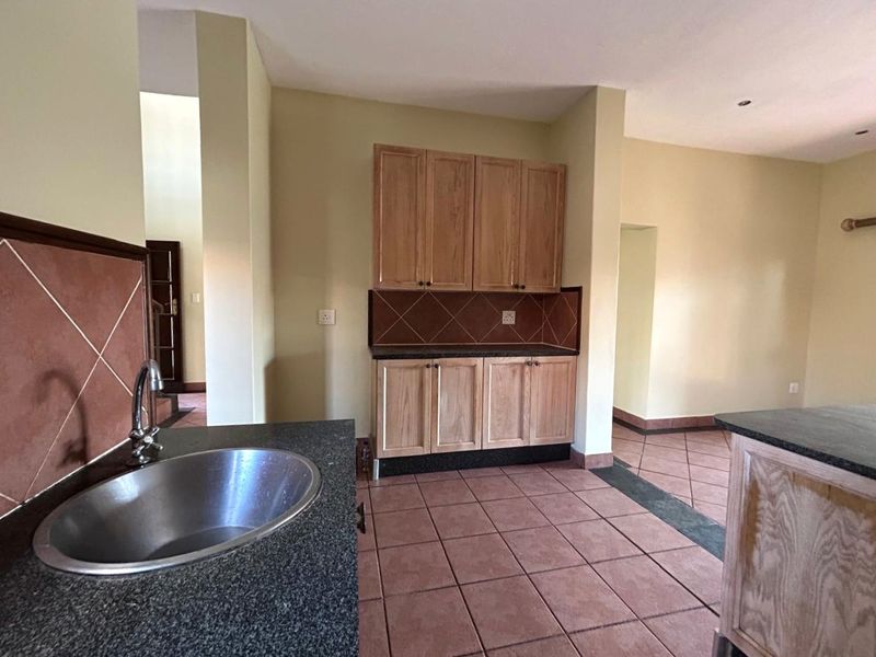 A functional kitchen area featuring built-in wooden cabinetry, granite countertops, a stainless steel sink, and tiled flooring throughout.