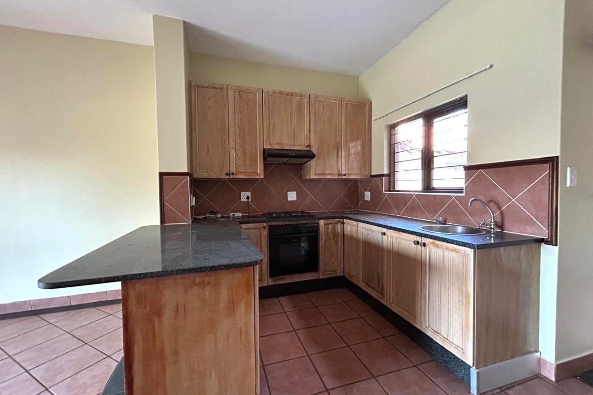 A functional kitchen featuring wooden cabinetry, granite countertops, built-in oven, gas hob, and tiled finishes throughout.