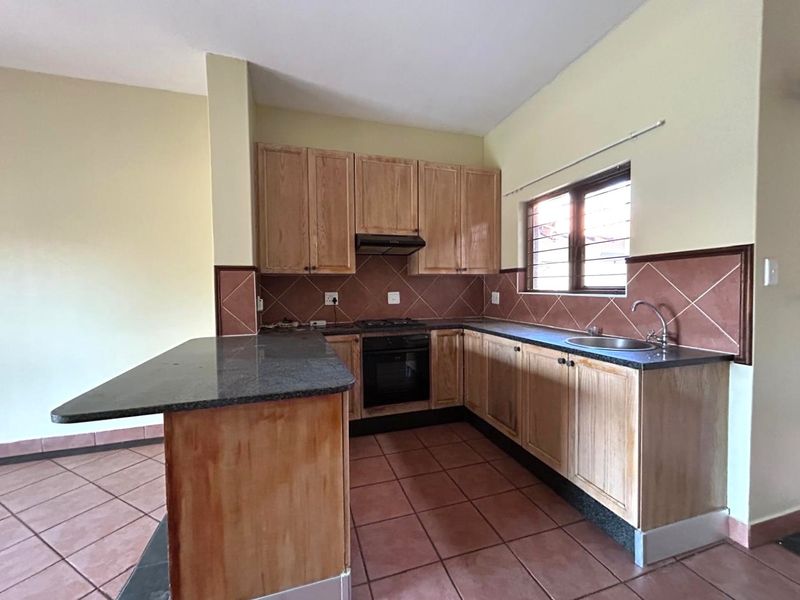 A functional kitchen featuring wooden cabinetry, granite countertops, built-in oven, gas hob, and tiled finishes throughout.