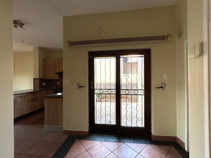 Open plan living area featuring tiled floors and a sliding door with security gate, leading to an outdoor space, adjacent to a fitted kitchen.