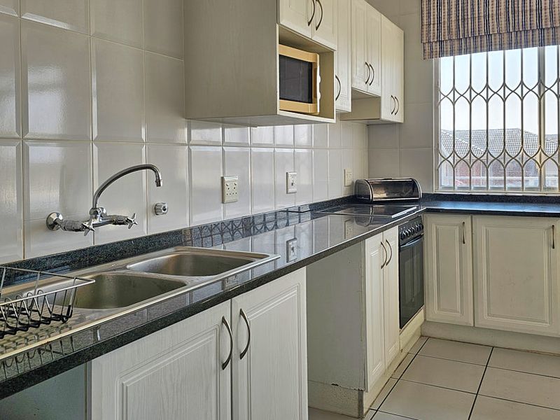 A functional kitchen featuring granite countertops, a double basin sink, built-in oven, microwave, and tiled finishes with security bars on the window.