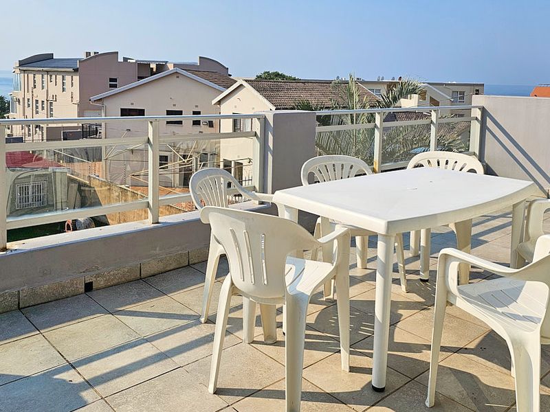 Spacious outdoor balcony featuring tiled flooring and a glass balustrade with metal railing, offering an elevated view of the surrounding neighborhood.
