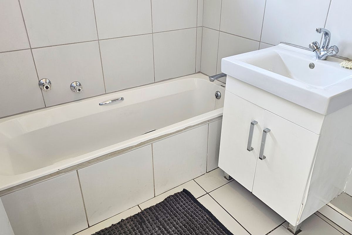 A functional bathroom featuring a white bathtub, a vanity cabinet with a basin, and neutral wall and floor tiling.