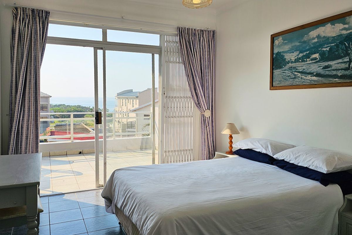 A bright bedroom featuring tiled floors and a large sliding glass door that opens onto a private balcony with coastal views.