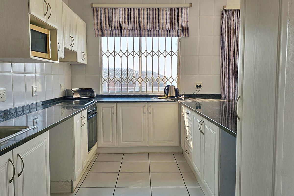 A functional kitchen featuring white cabinetry, dark granite countertops, tiled backsplash, and built-in oven, with natural light from a window with security bars.