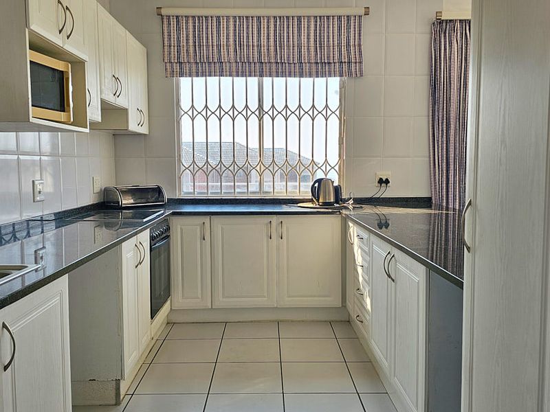 A functional kitchen featuring white cabinetry, dark granite countertops, tiled backsplash, and built-in oven, with natural light from a window with security bars.