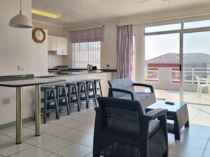 Open-plan living and kitchen area featuring tiled floors, a breakfast bar, and large sliding doors leading to a private balcony.