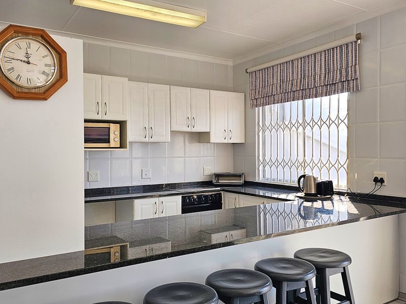 A functional kitchen featuring granite countertops, white cabinetry, built-in appliances, and a breakfast bar area with security window bars.