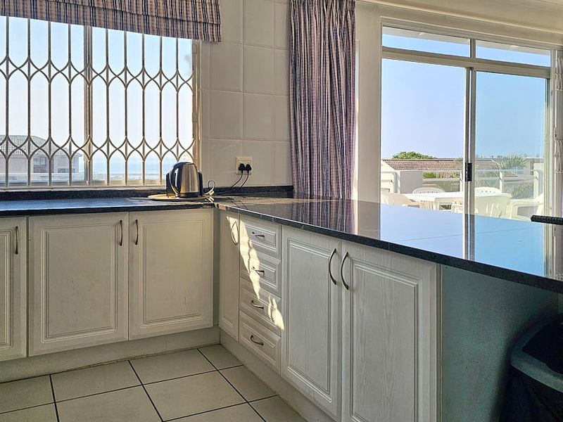 A functional kitchen featuring granite countertops, white cabinetry, tiled flooring, and direct access to an outdoor balcony area.
