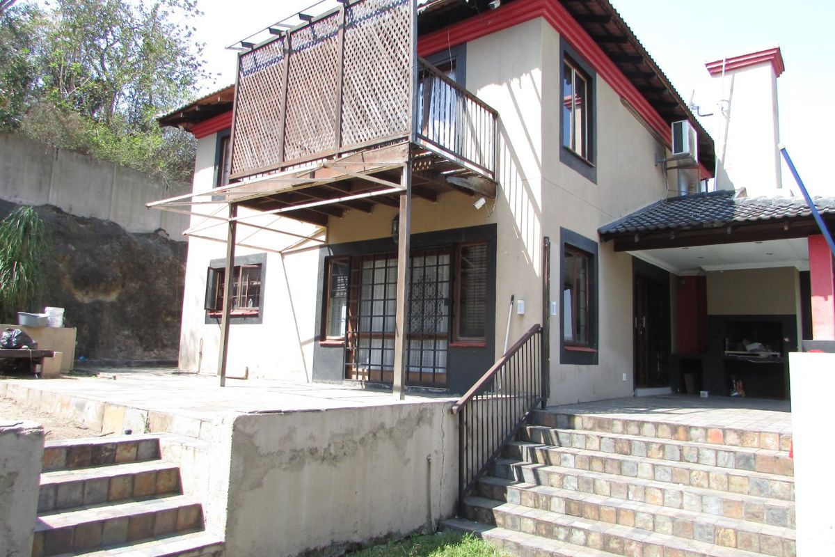 Rear view of a two-story house featuring a balcony, tiled patio area, built-in braai, and external staircase access.